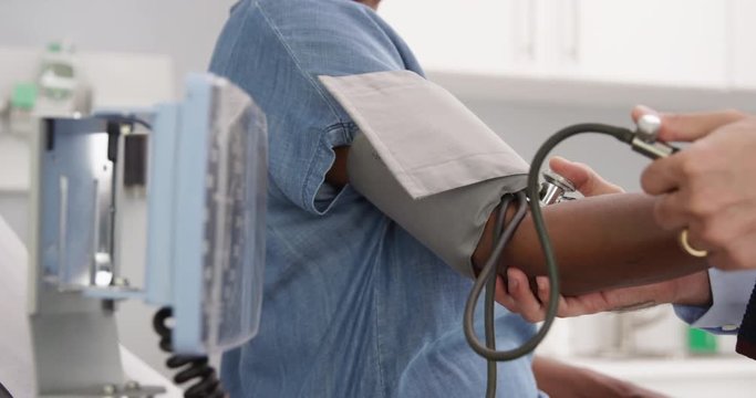 Close view of blood pressure monitor used on elder African woman. Close-up of doctor checking senior patients blood pressure with stethoscope