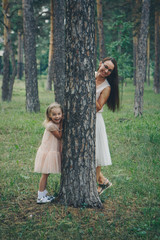 mom and daughter are hiding behind a tree. a woman and a little girl peeking out from behind a pine tree