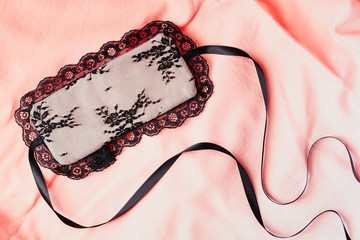 Beautiful female lace eye mask on a pink bedsheet.