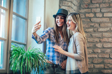 Portrait of young smiling female friends using smart phone, make selfie photo.