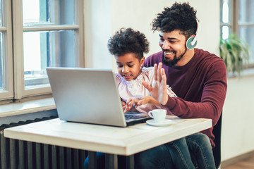 Young african american father siting together with his daughter, they are using a laptop. - Powered by Adobe