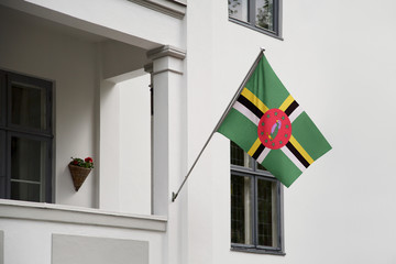 Dominica flag. Dominica flag hanging on a pole in front of the house. National flag of waving on a home displaying on a pole on a front door of a building. Flag raised at a full staff.
