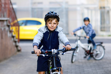 Two school kid boys in safety helmet riding with bike in the city with backpacks. Happy children in...