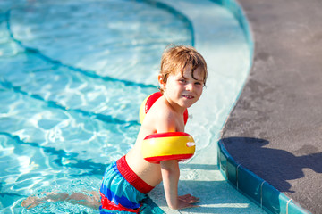 Happy little kid boy having fun in an swimming pool. Active happy child learning to swim. with safe floaties or swimmies. Family, vacations, summer concept