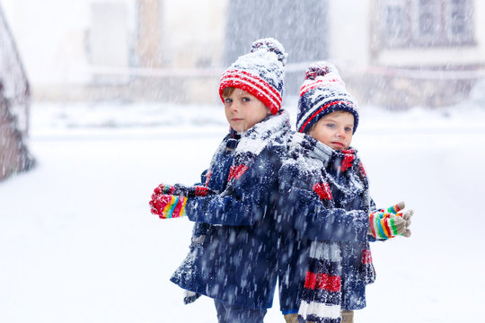 Two little kid boys in colorful fashion clothes playing outdoors during strong snowfall. Active leisure with children in winter on cold days. Happy siblings and twins having fun with first snow.