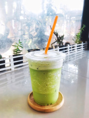 Green tea milk frappe in clear plastic glass have orange straw in wooden tray put on dining table...