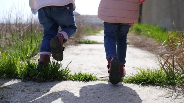 Two little kid girls legs in jeans walking down the concrete sidewalk path