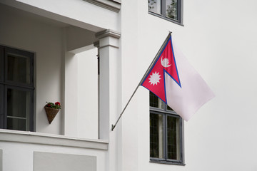 Nepal flag. Nepal flag hanging on a pole in front of the house. National flag of waving on a home displaying on a pole on a front door of a building. Flag raised at a full staff.