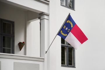 North Carolina flag.  North Carolina state flag hanging on a pole in front of the house. State flag waving on a home displaying on a pole on a front door of a building.Flag raised at a full staff.
