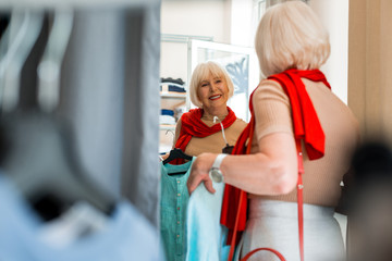Weekend shopping. Waist up of adorable elderly woman choosing summer dress in clothing store while...