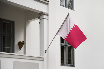 Qatar flag. Qatar flag hanging on a pole in front of the house. National flag of Qatar waving on a home displaying on a pole on a front door of a building. Flag raised at a full staff.