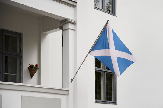 Scotland flag.  Scotch flag hanging on a pole in front of the house. National flag of Scotland waving on a home displaying on a pole on a front door of a building. Flag raised at a full staff.