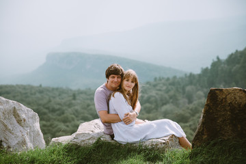 Young couple sitting on the edge of mountains with a beautiful view