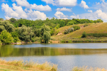 Summer landscape with beautiful lake, green meadows, hills, trees and blue sky