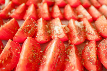 The manufacturing process of sundried tomatoes cut into slices sprinkled with salt, oregano, Basil, thyme being dried out in the sun or in the oven Close-up, selective focus.