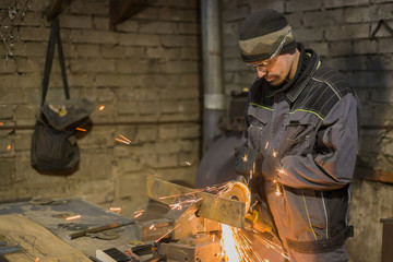 Fototapeta na wymiar Professional blacksmith sawing metal with hand circular saw at forge, workshop. Handmade, craftsmanship and blacksmithing concept