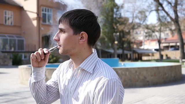 Portrait man smoking electronic cigarette breathing out smoke slow motion