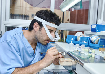 Dental technician working with ceramic dental implants with magnifying glasses