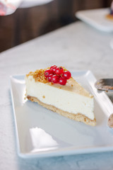 Cheesecake with red currant berries on white plate.