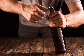 partial view of man opening beer bottle by opener at wooden table