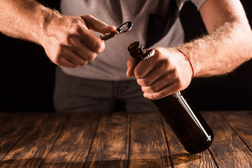 cropped image of man opening beer bottle by opener at wooden table