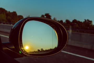 Yellow sun shining on a right mirror black car