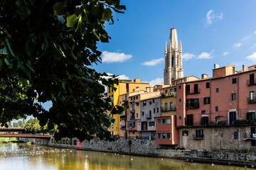 Fototapeta na wymiar Girona's landmark cathedral and river houses on a sunny blue sky and green foliage canvas