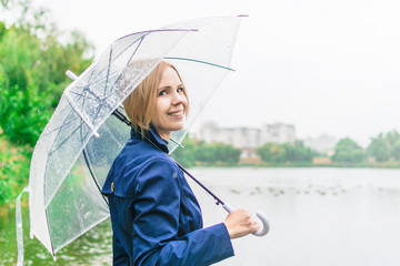 A woman of 30-40 years old smiles in a blue raincoat under a transparent umbrella in the autumn...