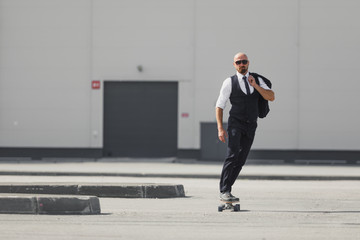 Confident young businessman in business suit on longboard hurrying to his office, on the street in the city