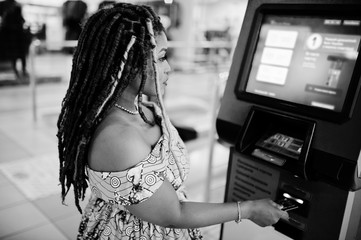 Cute small height african american girl with dreadlocks, wear at coloured yellow dress, against ATM...