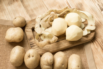 Raw tubers peeled potatoes on a wooden background.