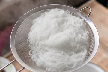 Boiled hot steaming rice noodles, spaghetti in a colander.