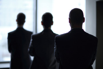 back view three employees as they look out on a large window overlooking the city