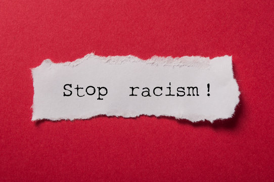 closeup of white torn paper on red paper background - Stop racism !