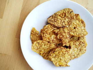 Fried tempeh in a white plate on the wooden surface. 