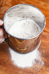 sifting the flour through sifter on wooden table
