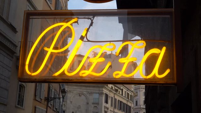 CLOSE UP: Vintage lettering glowing outside of a traditional pizza shop in Rome. Cool shot of retro yellow pizza sign shining brightly in an empty alley in a big city in Italy. Popular Italian food.