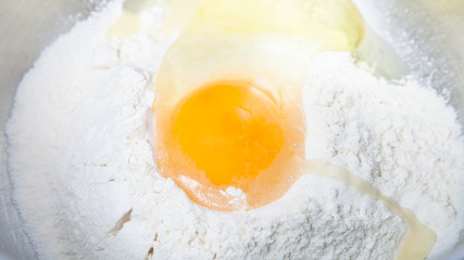 pile of flour with broken egg close up in bowl