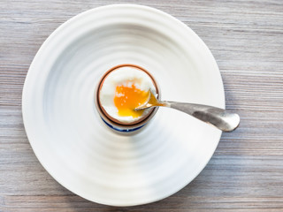 soft-boiled brown egg with spoon in cup on plate