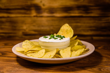 Ceramic plate with potato chips and glass bowl with sour cream on wooden table