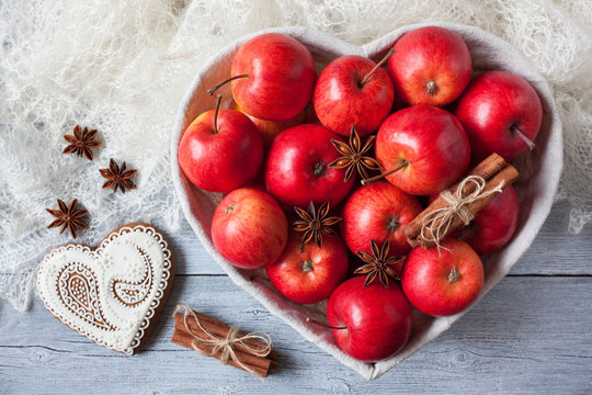 Red apples, cinnamon, anise in a basket in the shape of a heart on a table