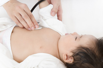 病院で胸に聴診器を当て診察を受ける新生児の赤ちゃん。子供の健康診断、健診,定期健診,診察,病気イメージ