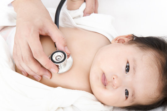 病院で胸に聴診器を当て診察を受ける新生児の赤ちゃん。子供の健康診断、健診,定期健診,診察,病気イメージ