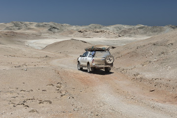 Obraz na płótnie Canvas ein Geländewagen fährt durch eine Mondlandschaft, Namibia