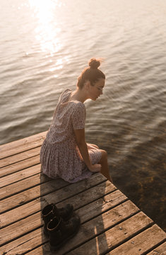 Young caucasian girl sitting and relaxing on a dock of a lake in a sunset of summer mountains background