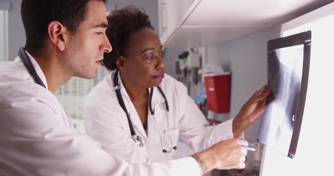 Senior African radiologist consulting with young Hispanic colleague over patient x rays. Two medical doctors reviewing patient x-ray of patients spine and skull