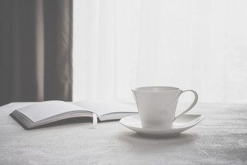 cup of coffee, a plaid notebook on the table in front of a window with a copy space