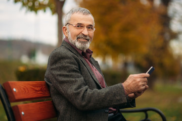 Fototapeta premium Grandpa uses a tablet sitting in the park on the bench