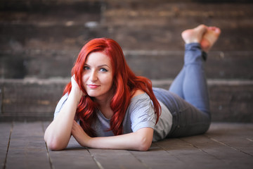 Young woman with red long hair indoor portrait lies on wooden floor