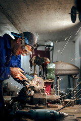 mechanic in blue uniform, cuts the steel part with an angle grinder in the workshop. the concept of protection technology in the workplace, eye protection. sparks fly in the eye, vertical photo